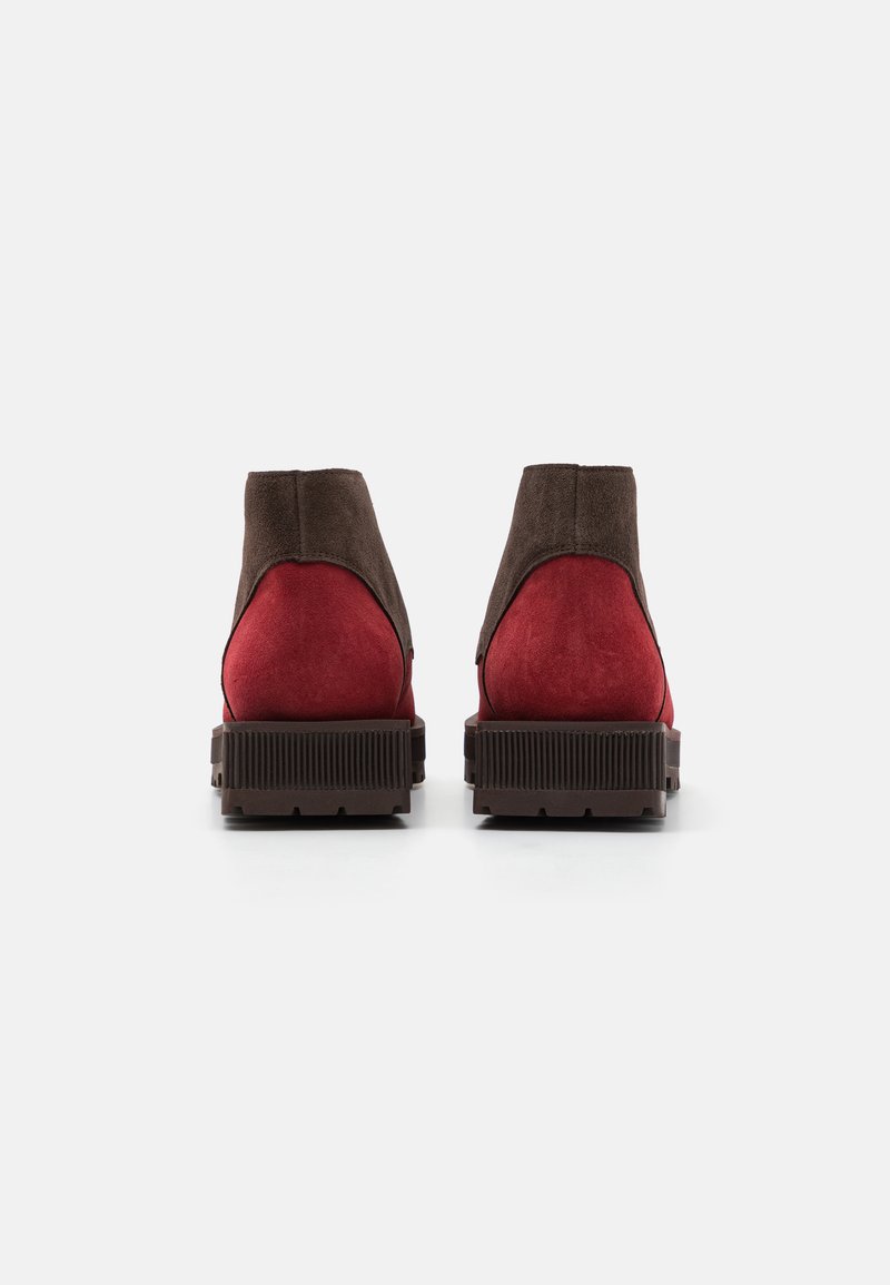 Stivali alla caviglia in suede con tomaia marrone e parte inferiore rossa; presentano una suola in gomma marrone con texture e un design elegante e arrotondato.