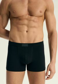 Czarne bokserki o gładkiej fakturze, dopasowanym kroju i markowym pasku w talii. Materiał jest miękki i elastyczny dla wygody.