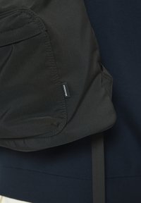 Sac à dos en tissu noir avec poche avant et étiquette "Martinique" sur fond bleu foncé.