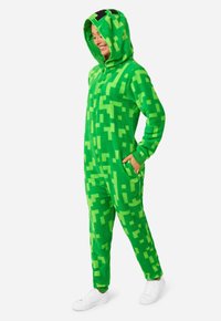 Green plush onesie with a pixelated pattern, zip closure, and hood. Features two side pockets and elastic cuffs. Accented with black details.