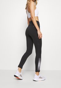 Svarta sportleggings med hög midja, med en texturerad sidremsa och detaljer vid anklarna. Matchas med en vit sport-bh och skor.