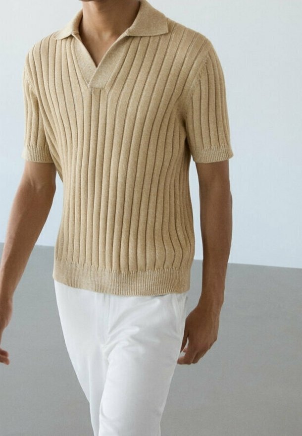 Polo en tricot beige avec texture côtelée verticale, manches courtes et col plat, associé à un pantalon blanc.