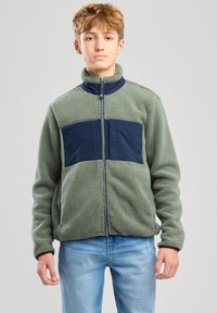 Fleece jacket in light green with navy accents, zip closure, high collar, and two front pockets. Soft texture and relaxed fit.