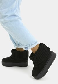 Bottines noires avec un col en tricot côtelé, une doublure intérieure douce et une semelle en caoutchouc épaisse ; assorties à un jean en denim bleu clair retroussé.