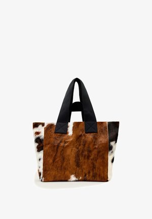 Tote bag met een koeienhuidpatroon in bruin, wit en zwart en brede zwarte stoffen handvatten op een witte achtergrond.