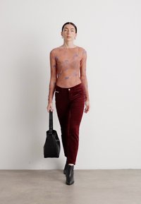Ilga rankovė, permatomas, raštuotas viršus persikų spalvos su mėlynomis detalėmis; raudonai rudos aksominio medžiagos kelnės; juodi odiniai batai ir rankinė. Minimalistinės estetikos.