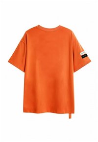 Camiseta de algodón naranja con cuello redondo, mangas cortas y un discreto detalle de etiqueta lateral. Textura suave y corte relajado.