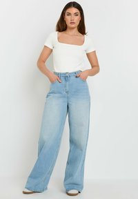 Top bianco aderente con maniche corte e scollo quadrato, abbinato a jeans a gamba larga azzurri a vita alta. Texture liscia e design casual.
