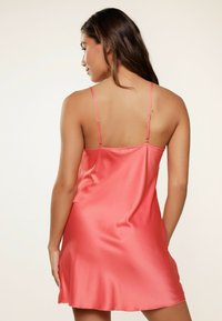 Vestido de seda en color coral vibrante, con tirantes finos ajustables y un dobladillo fluido, que resalta una textura suave.