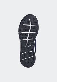 Semelle de chaussure Adidas noire et blanche avec motifs de bande de roulement texturés et marquage "Adiwear" sur fond gris clair.