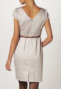 Abito a pois in tessuto beige, con scollo a V sul retro, maniche corte e una cintura marrone in vita. L'abito ha una vestibilità slim e una ventola sul retro.