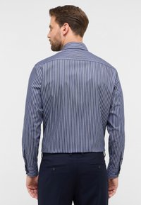 Camicia a righe blu navy con maniche lunghe, strisce verticali bianche a contrasto, bottoni ai polsini e colletto standard. Presenta una texture liscia.