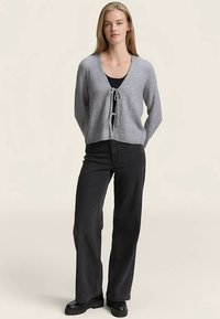 Szürke kötött kardigán V-nyakú és húzózsinóros záródással, fekete bő szárú nadrággal és fekete csizmával párosítva, sima textúrával.