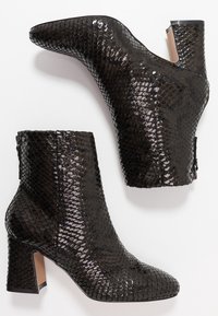 Botas negras hasta el tobillo con una textura de piel de serpiente brillante. Con puntera afilada y tacón cuadrado, y cierre con cremallera lateral.