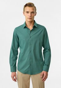 Groene kraagloze button-up shirt met lange mouwen, gemaakt van een gladde stof, met een subtiele glans en een afgeronde zoom. Klassiek ontwerp met knopen.