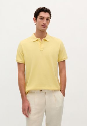 Geel poloshirt met korte mouwen, lichtgewicht stof, met een knoopsluiting van twee knopen, gecombineerd met lichtbeige broeken. Eenvoudig, strak ontwerp.