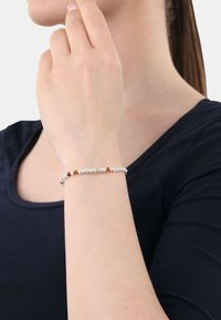 Pulsera de cuentas con cuentas plateadas y marrones, exhibida en una muñeca, con una textura suave y un diseño sencillo.