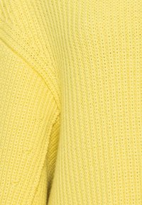 Gros plan sur un tissu tricoté doux de couleur jaune montrant les motifs de points et la texture en détail.