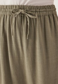 Jupe légère de couleur vert olive avec une taille élastique et un cordon de serrage. Le tissu a une texture subtile, tombant en drapés doux.