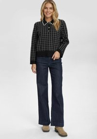 Pull en maille à carreaux noirs avec col, associé à un pantalon en denim large de couleur foncée et des bottines à talons tan. Texture douce et design ajusté.
