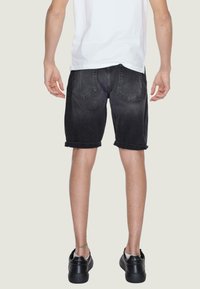 Shorts in denim nero con risvolti, due tasche sul retro e una finitura sbiadita, abbinati a sneakers nere e una t-shirt bianca.