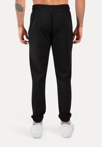 Sorte sweatpants med elastisk talje, tapered ben og ribbede manchetter. Båret med hvide sneakers, der har sorte snørebånd og branding.