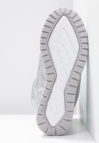 Šedé tenisky s texturovanou gumovou podrážkou, hladkým svrchním materiálem a výrazným vzorem podrážky. Čistý design, minimální akcenty.