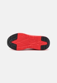 Red and black athletic shoe sole featuring a textured pattern for grip, prominent grooves, and a reinforced heel area.