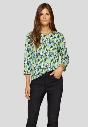Long-sleeve, loose-fitting top in a vibrant abstract green, blue, and white pattern, paired with black denim jeans. Smooth fabric texture.