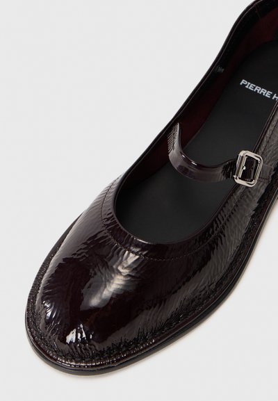Chaussures en cuir verni bordeaux avec un bout arrondi, bride Mary Jane et des coutures détaillées le long de la semelle. Texture lisse et brillante.