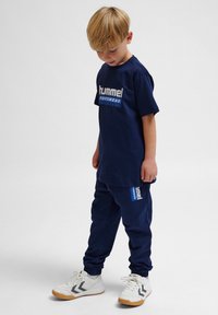 Marineblå jersey t-shirt og sweatpants sæt med "hummel SPORTSWEAR" logo. 100% bomuldsmateriale, afslappet pasform, elastiske manchetter og hvide sneakers.