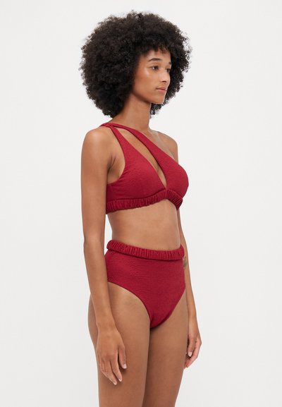 Punane tekstureeritud bikiinikomplekt, mis sisaldab bralette'i asümmeetriliste rihmade disainiga ja kõrge vöökohaga aluspükse volangiga vööl.