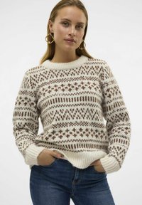 Strickpullover in Creme und Braun. Verfügt über geometrische Muster, einen runden Halsausschnitt und gerippte Bündchen. Weiche Textur, kombiniert mit blauen Jeans.