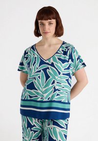 Maglietta a maniche corte con scollatura a V, caratterizzata da uno sfondo blu e un grande motivo di foglie verdi e bianche, completata da accenti a righe all'orlo.