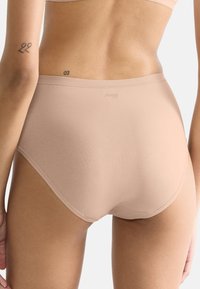 Close-up van een persoon die naadloze huidkleurige high-waistedondergoed en een bijpassende beha draagt, met de achterkant en het midden van het lichaam zichtbaar, waarop kleine tatoeages op de huid zijn te zien.