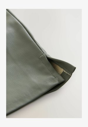 Zelený kožený produkt s hladkou textúrou, s čistými okrajmi a viditeľným prešívaním. Obsahuje malý záhyb na otvore pre detail.