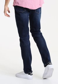 Mörkblå denimjeans med smal passform, femficksdesign och subtila blekningar, kombinerade med vita sneakers med svarta detaljer.