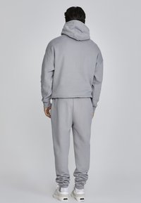 Set di felpa e pantaloni della tuta grigi, realizzato in tessuto morbido, con tasca a marsupio, vestibilità rilassata e polsini a coste. Cappuccio grande sul retro.