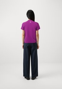 Camiseta corta de manga corta morada con dobladillo redondeado, combinada con pantalones navy de corte holgado y zapatos negros. Diseño minimalista.