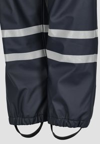 Marineblauw waterdicht buitenstof met twee horizontale reflecterende strepen en elastische manchetten. Voorzien van verstelbare banden voor een goede pasvorm.