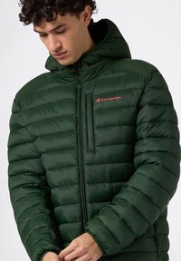 Zielona pikowana kurtka z zapięciem na zamek, z kapturem i przednią kieszenią. Logo "Champion" w czerwonym kolorze na klatce piersiowej. Gładka, błyszcząca faktura.