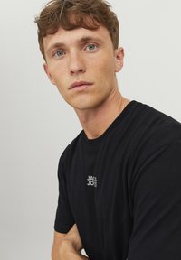 Sort bomulds T-shirt med rund hals, korte ærmer og et lille, hvidt logo på brystet. Blød tekstur og afslappet design.