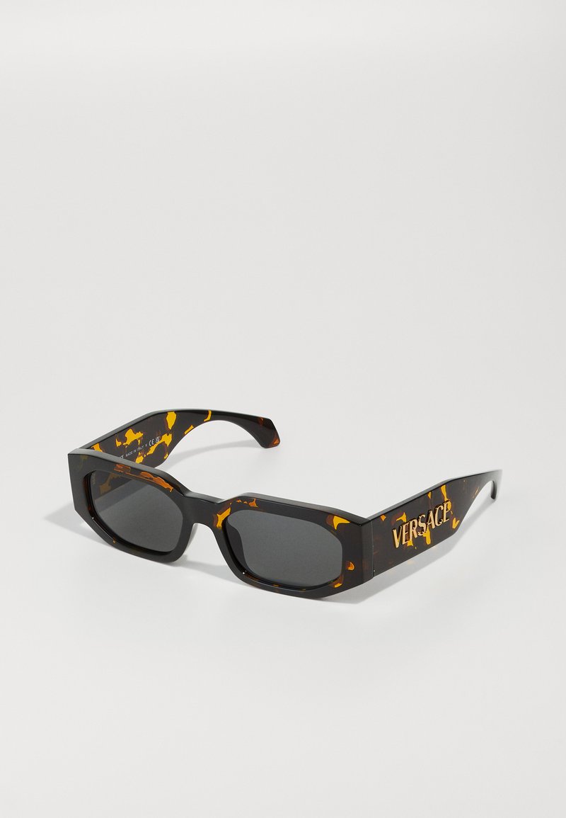 Versace sunglasses with a brown tortoiseshell frame and gradient black lenses. Features bold logo on the temples and a chunky angular design.