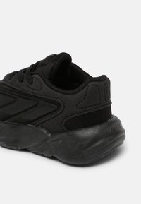 Zapatilla deportiva negra con parte superior de tela texturizada, suela de goma suave, diseño de cordones y sutiles acentos negros en el costado.