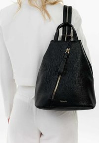 Zwarte leren rugzak met een gestructureerde afwerking, taps toelopende vorm, dubbele handgrepen bovenaan en een voorste ritsdetail, die een minimalistisch ontwerp laat zien.