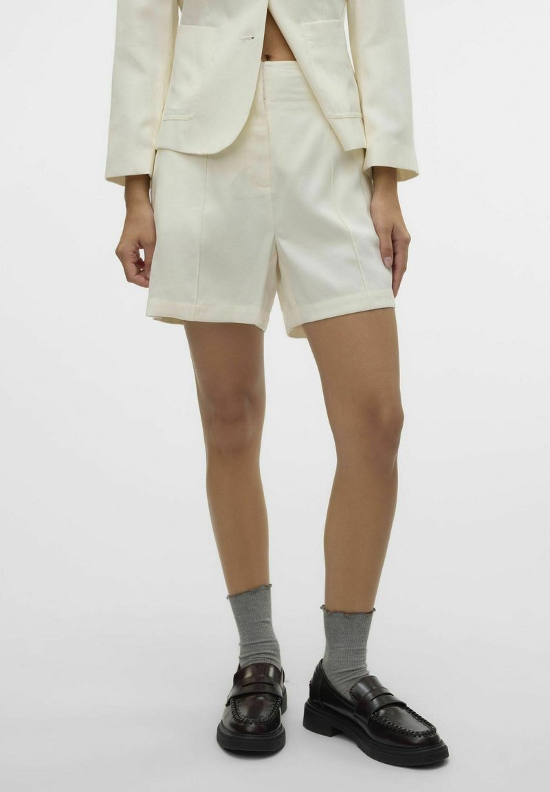 Pantaloni corti bianchi su misura con un taglio dritto, caratterizzati da un design elegante e hardware minimal. Abbinati a mocassini scuri e calzini alla caviglia grigi.