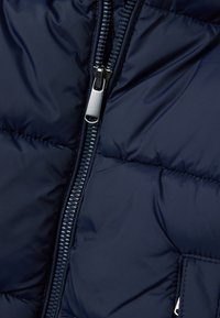 Giacca puffer blu navy con zip lucida, texture trapuntata e tasche laterali, realizzata in tessuto resistente e dal finish liscio.