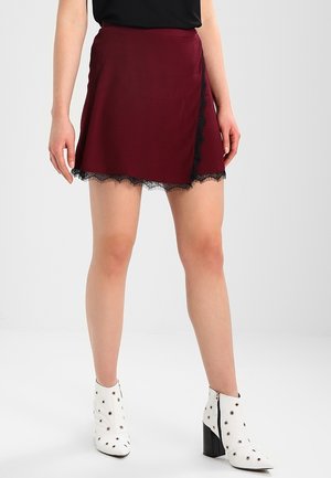 Bordowa spódnica z koronkowym wykończeniem na dole, o asymetrycznym kroju. Noszona z białymi botkami za kostkę ozdobionymi metalowymi ćwiekami.