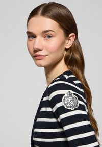 Marinblå och vit randig stickad tröja med rund halsringning och ett märke på vänster ärm som har en krona och emblem.