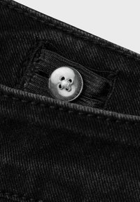 Mustaka denim-kangas, jossa on hopeinen nelireikäinen nappi vyötäröllä. Näkyvät ompelu yksityiskohdat ja sileä pinta.